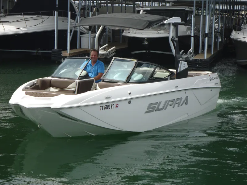 Slide: The Image of 2018 Supra SL boat on water with driver, docked boats in background. - 5
