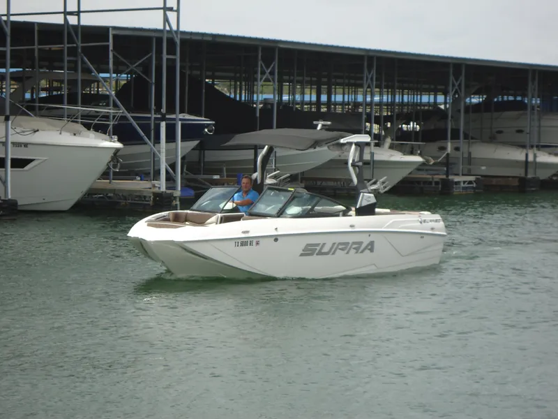 Slide: The Image of 2018 Supra SL boat cruising near a marina. - 7