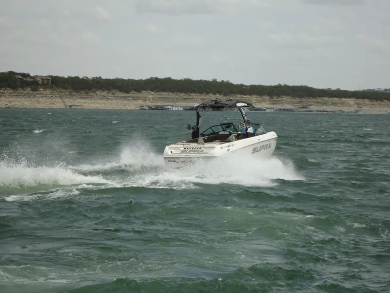 Slide: The Image of 2018 Supra SL boat cruising on a lake with a scenic shoreline. - 9