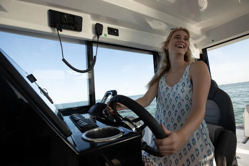 Slide: The Image of 2024 Jeanneau NC 895 Sport, woman steering boat, enjoying sunny day on the water. - 15