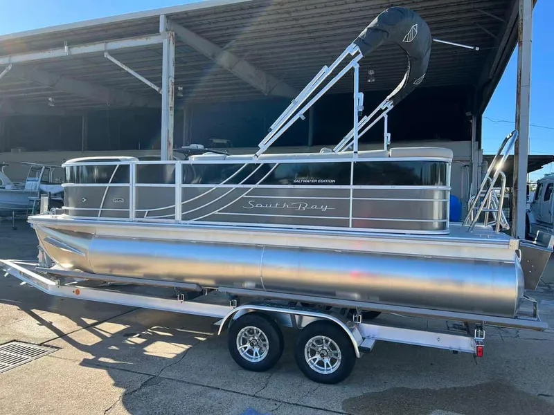 Slide: The Image of 2023 South Bay 220CR LE 2.0 pontoon boat on a trailer in a marina. - 2