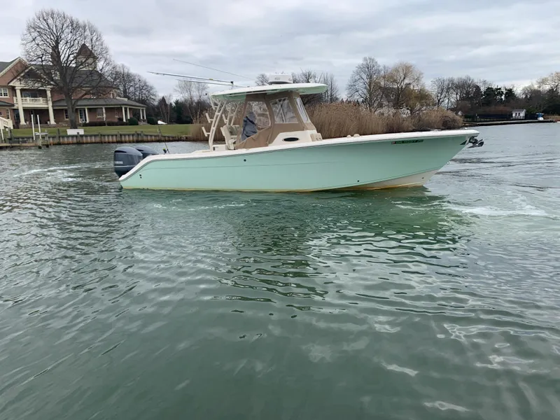 Slide: The Image of 2016 Cobia 296 CC boat cruising on a calm lake near a house. - 5