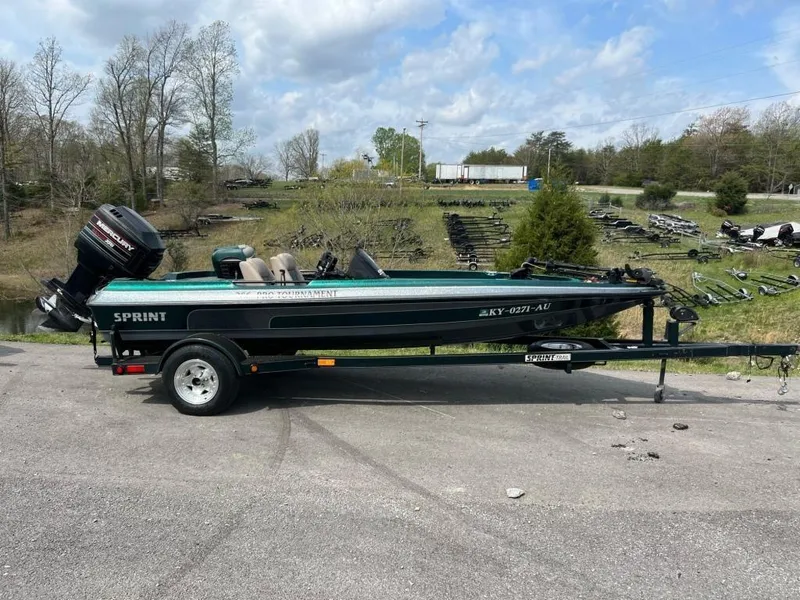 The Image of 1999 Sprint 286 Pro boat on trailer with outboard motor in a rural setting. - 0