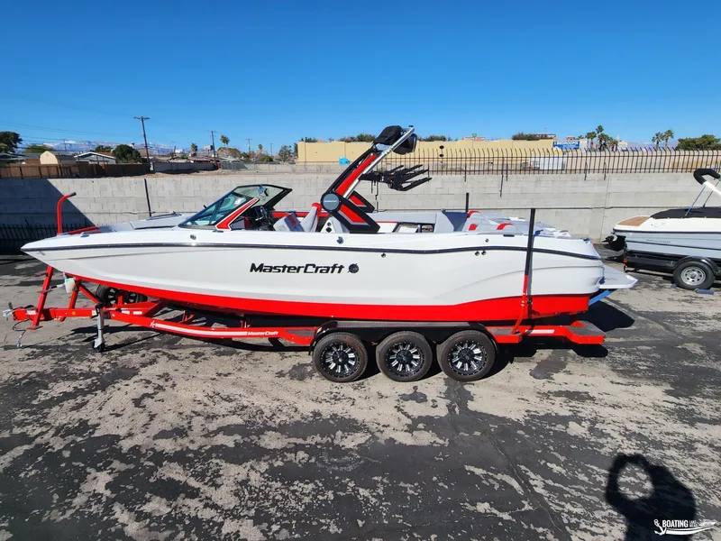Slide: The Image of 2023 MasterCraft X26 boat on a red trailer, parked outdoors. - 0