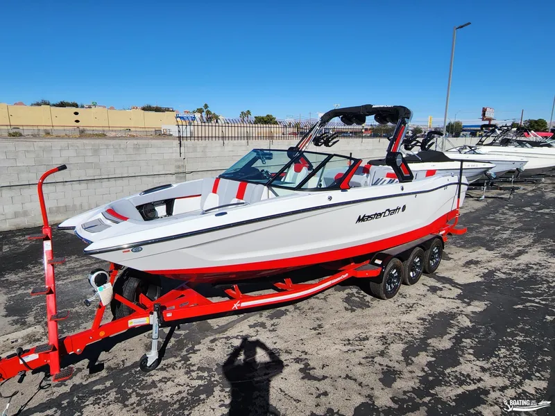 Slide: The Image of 2023 MasterCraft X26 boat on red trailer, parked outdoors. - 1