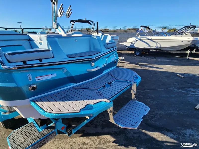 Slide: The Image of 2023 MasterCraft XStar S boat with blue exterior and swim platform in a marina. - 12