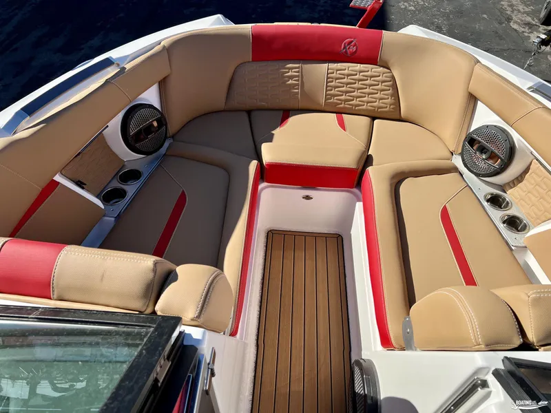 Slide: The Image of 2023 MasterCraft X24 boat interior with tan and red seating, wood flooring, and speakers. - 5