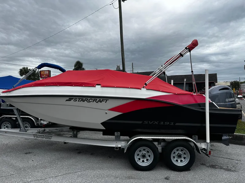 Slide: The Image of 2023 Starcraft SVX OB 191 boat with red cover on trailer, parked outdoors. - 0
