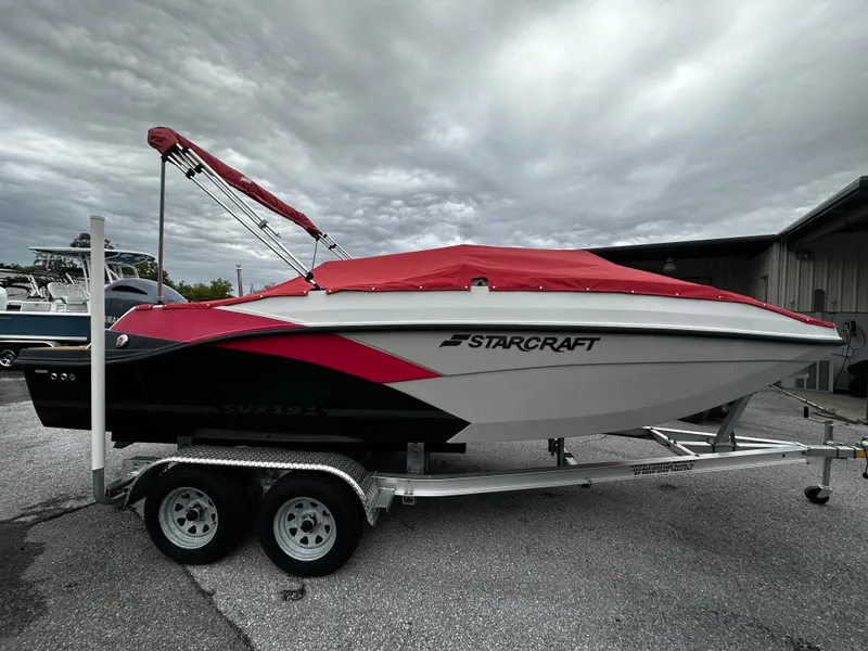 Slide: The Image of 2023 Starcraft SVX OB 191 boat with red cover on trailer, parked outdoors. - 3