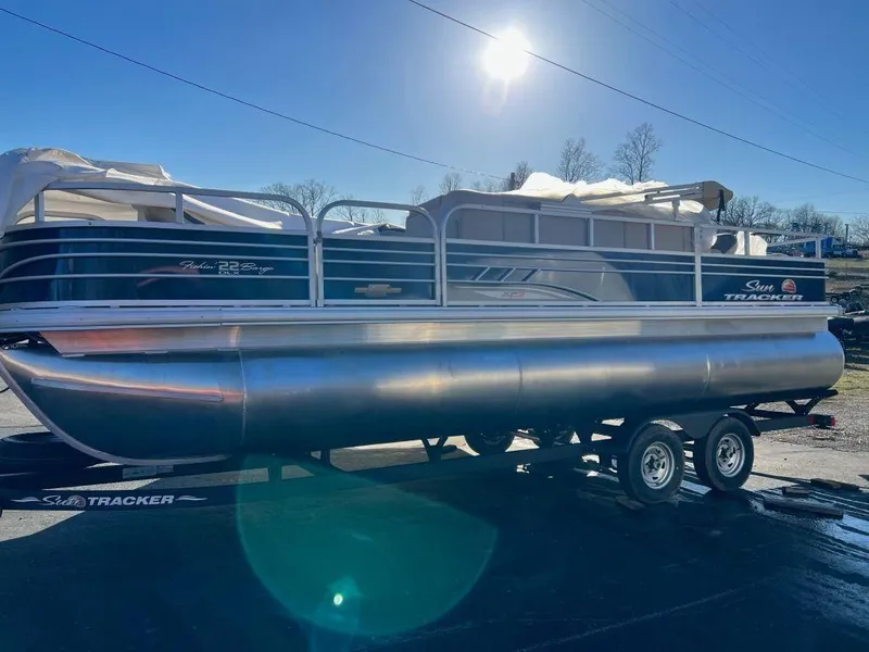 The Image of 2023 Sun Tracker FISHIN' BARGE® 22 XP3 pontoon boat on trailer under bright sun. - 1