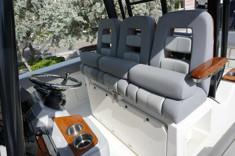 Slide: The Image of 2024 Boston Whaler 360 Outrage helm seating with gray cushions and wooden accents. - 15