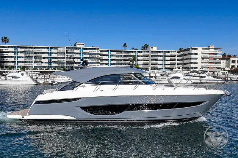 Slide: The Image of 2026 Riviera 4600 Sport Yacht Platinum Edition cruising in a marina with modern buildings. - 8