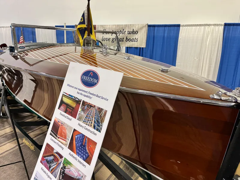 Slide: The Image of 1932 Hacker-Craft Triple Cockpit boat displayed with informational sign at a boat show. - 16