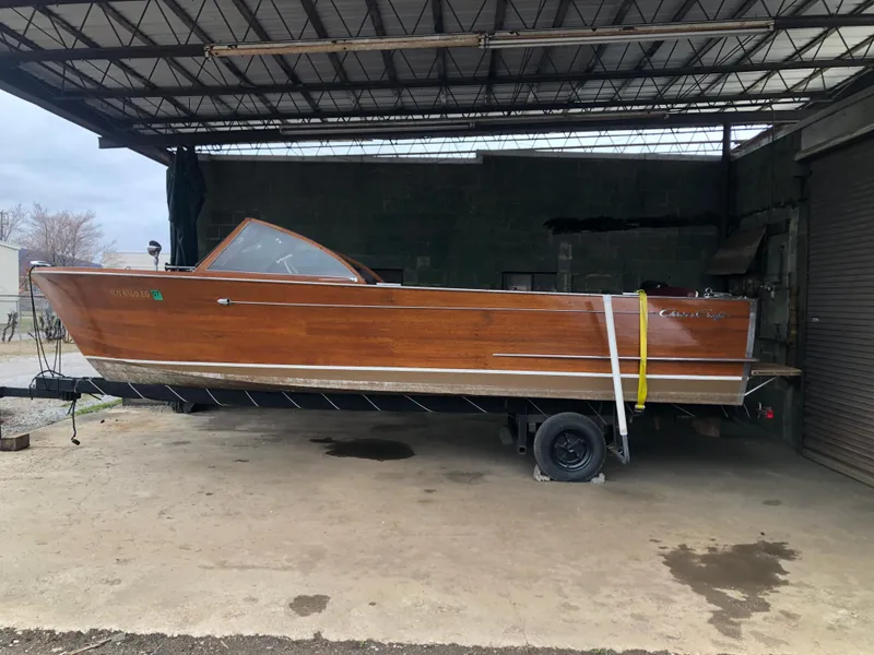 The Image of 1960 Chris-Craft 24 Sportsman wooden boat on a trailer in a covered area. - 1