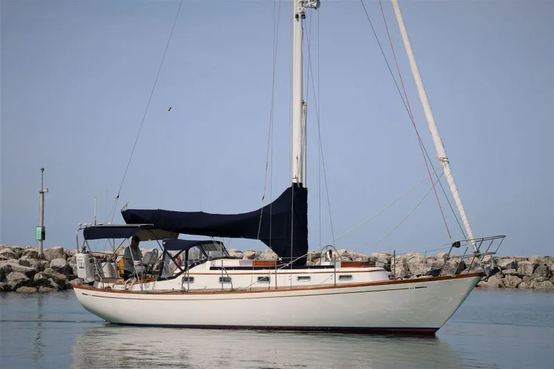 The Image of 1986 Mason 33 sailboat anchored near rocky shoreline under clear sky. - 0