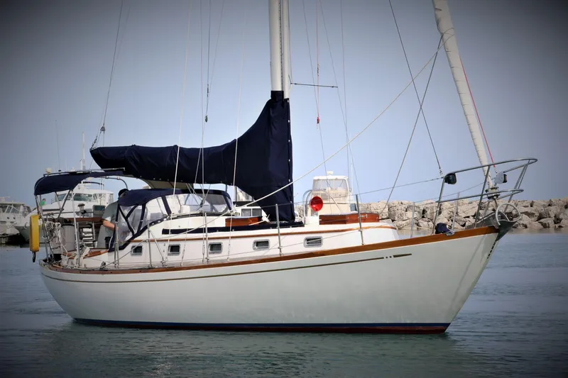 Slide: The Image of 1986 Mason 33 sailboat with dark blue sails docked in a marina. - 2