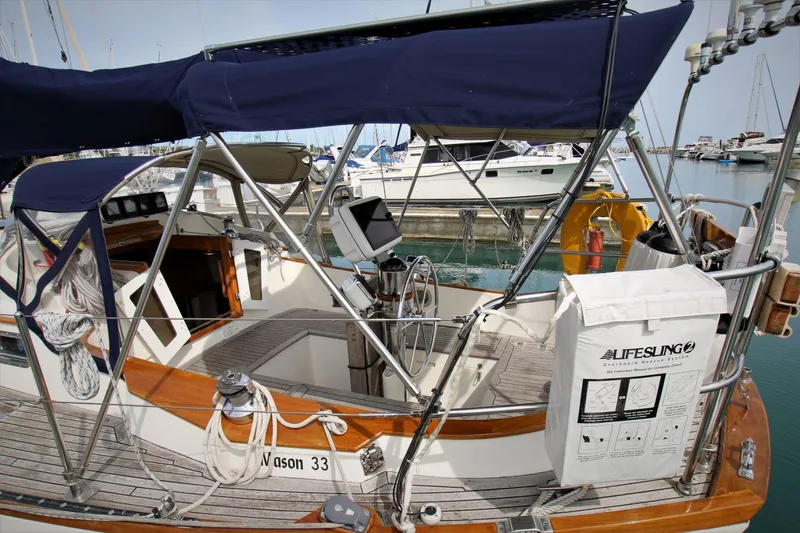 Slide: The Image of 1986 Mason 33 sailboat with blue canopy, docked in marina, featuring Lifesling safety equipment. - 21