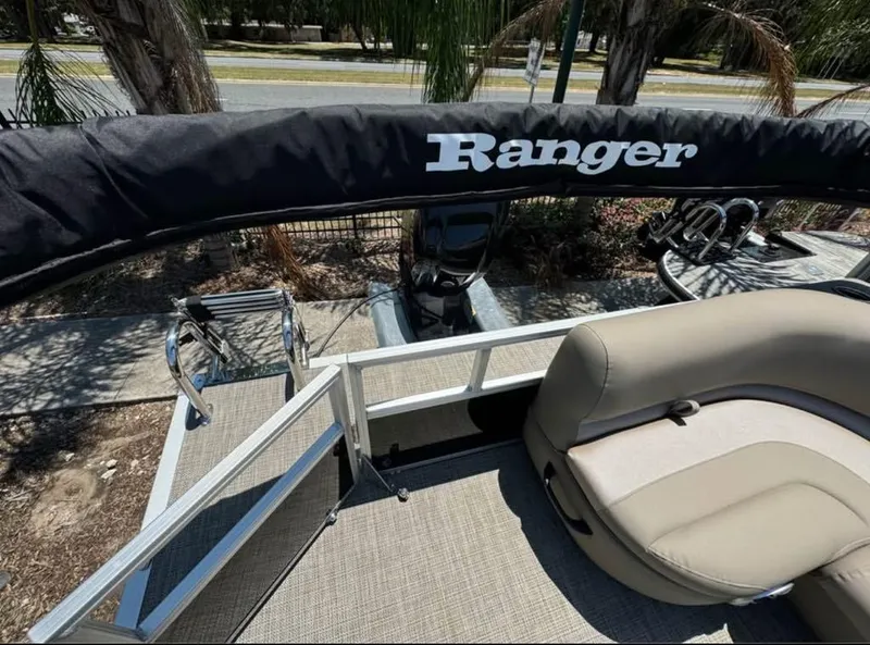 Slide: The Image of 2024 Ranger Reata 200C boat interior with seating and covered motor, parked near palm trees. - 2