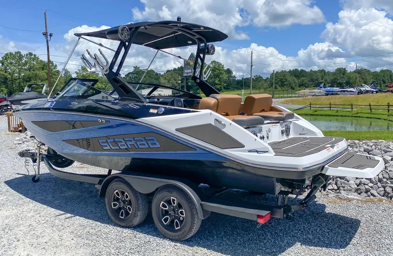 Slide: The Image of 2022 Scarab 215 ID Wake boat on a trailer, black and white exterior, sunny day. - 18