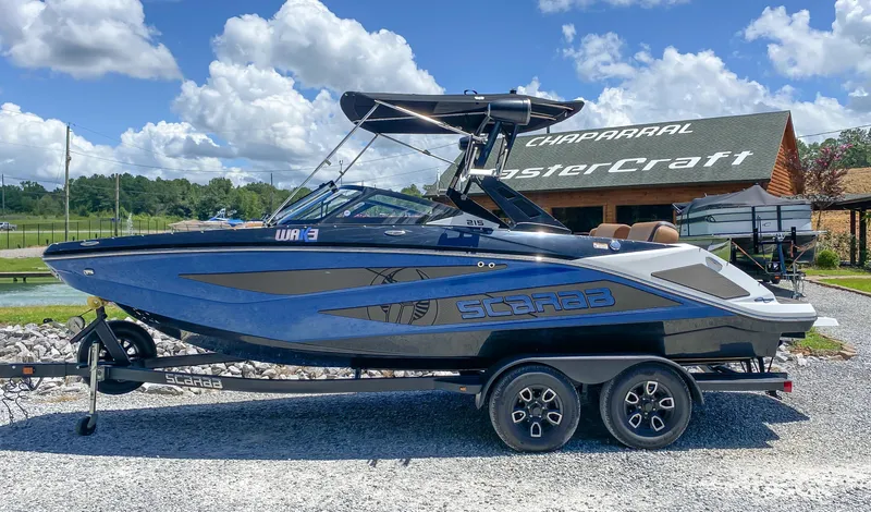 Slide: The Image of 2022 Scarab 215 ID Wake boat on a trailer, parked outdoors. - 2