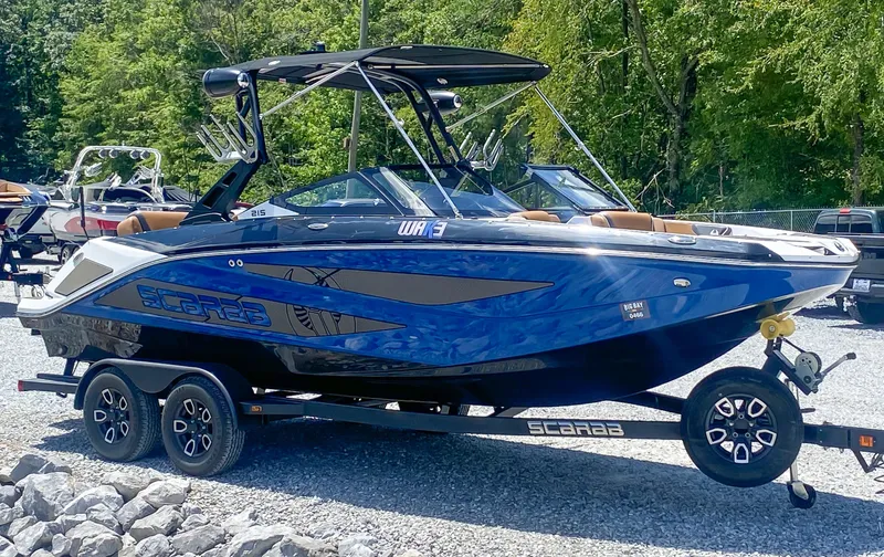 Slide: The Image of 2022 Scarab 215 ID Wake boat on trailer, blue and black, parked outdoors. - 21