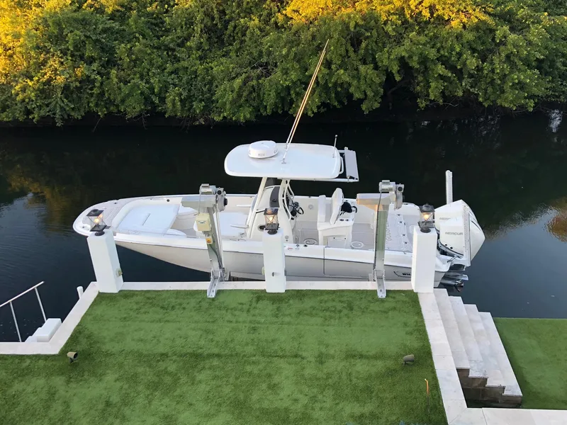 Slide: The Image of 2021 Boston Whaler Dauntless 27 boat docked on a lift by a lush green shoreline. - 0