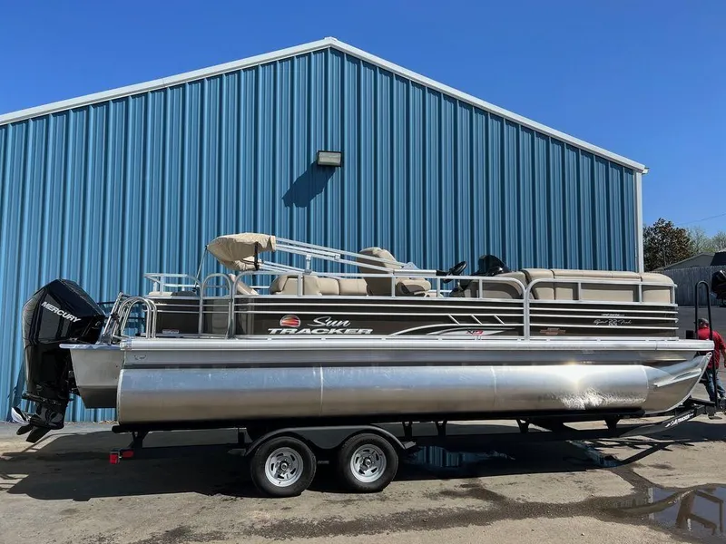 The Image of 2023 Sun Tracker SportFish™ 22 XP3 pontoon boat parked outside blue building. - 1