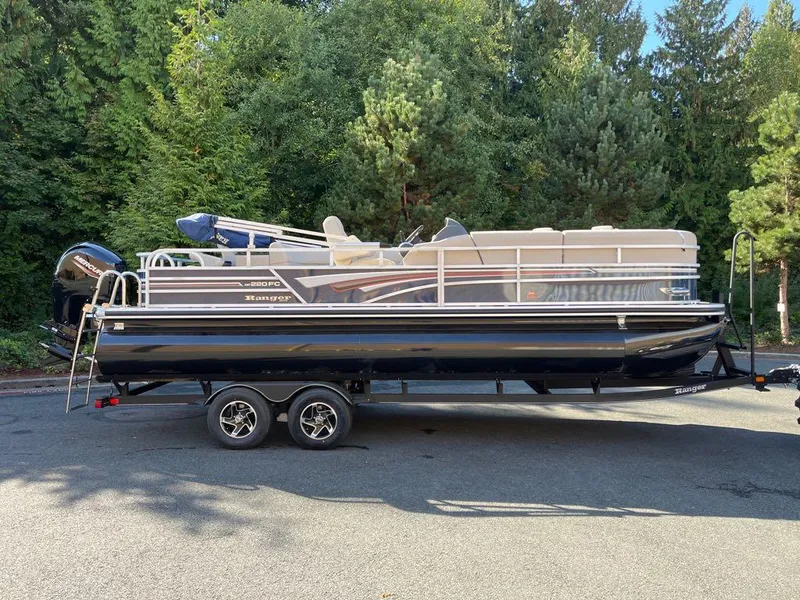 The Image of 2023 Ranger Reata 220FC pontoon boat on a trailer, parked near a forest. - 0