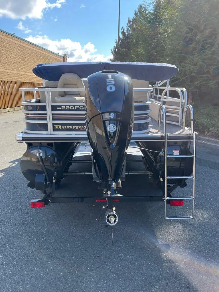 Slide: The Image of 2023 Ranger Reata 220FC pontoon boat on a trailer in a wooded area. - 3