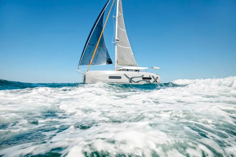 Slide: The Image of 2024 Excess 11 sailboat navigating ocean waves under clear blue sky. - 11