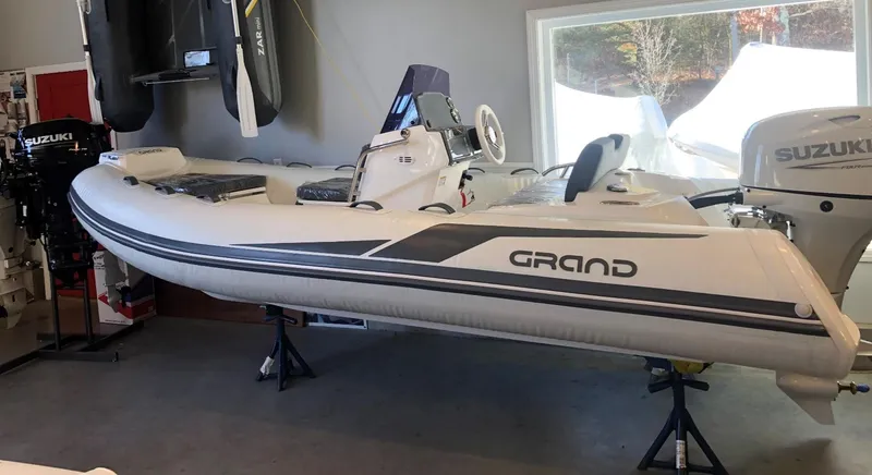 The Image of 2023 Grand 420 inflatable boat displayed indoors with Suzuki outboard motor. - 1