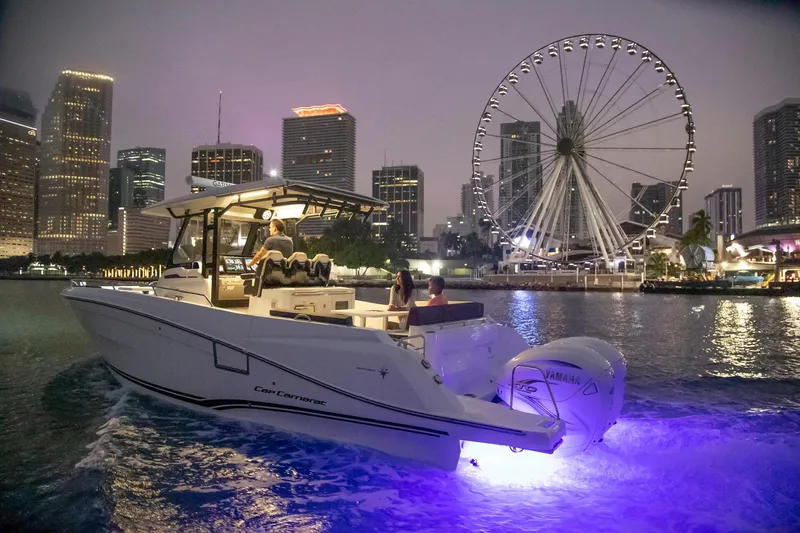Slide: The Image of 2024 Jeanneau Leader 10.5 CC boat cruising at night with city skyline and Ferris wheel. - 2