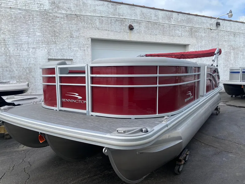 Slide: The Image of 2023 Bennington 21 SXSB pontoon boat with red exterior, docked near a white brick building. - 2