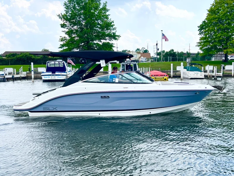 Slide: The Image of 2023 Sea Ray SLX 260 boat cruising on a lake near a marina. - 11