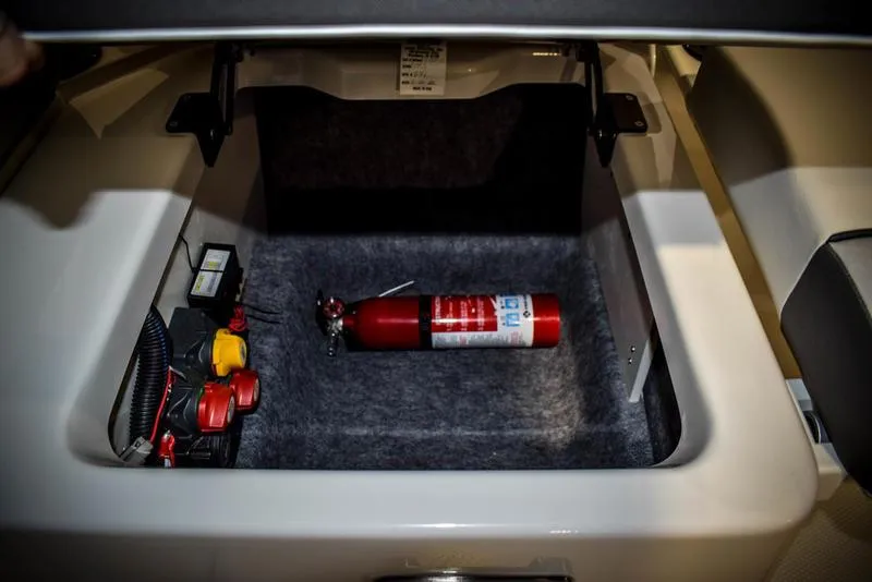 Slide: The Image of 2023 Yamaha Boats AR220 storage compartment with fire extinguisher and battery components. - 19