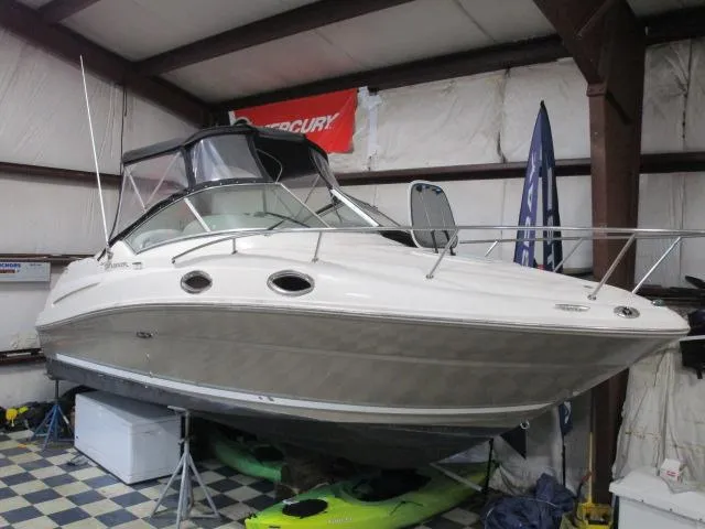 The Image of 2006 Sea Ray 240 Sundancer boat on trailer, parked near trees. - 1