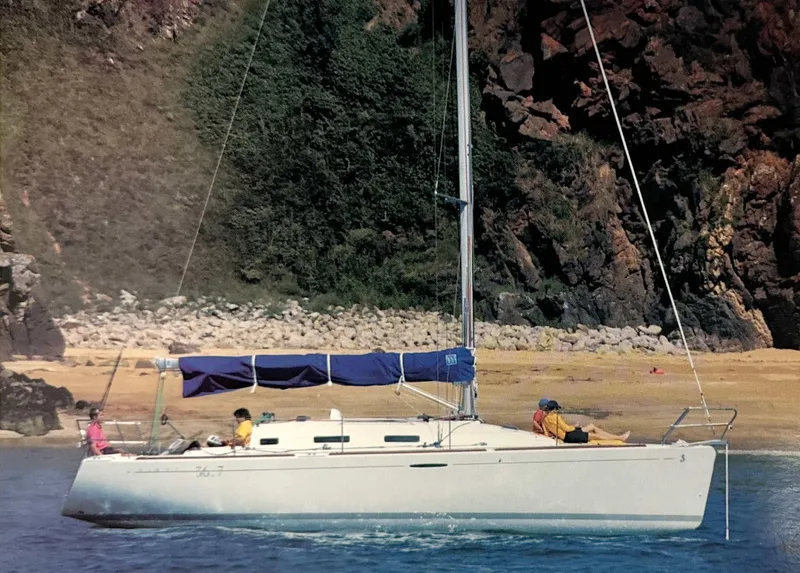 Slide: The Image of 2003 Beneteau First sailboat anchored near rocky shoreline with lush greenery. - 0
