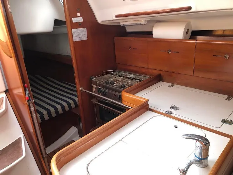 Slide: The Image of 2003 Beneteau First yacht interior with kitchen, stove, and striped bedding. - 12
