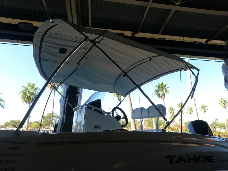 Slide: The Image of 2023 Tahoe 2150 CC boat with canopy, parked indoors, palm trees visible outside. - 3