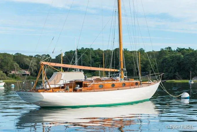 The Image of 1929 Herreshoff Fishers Island 31 sailboat on calm water, surrounded by lush greenery. - 0