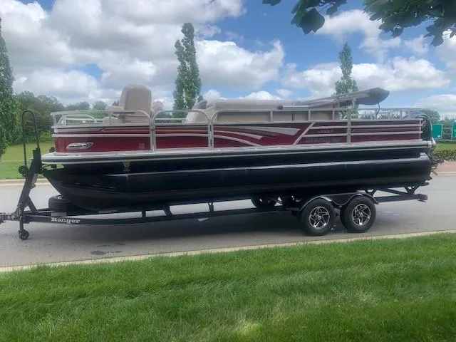 Slide: The Image of 2023 Ranger 223F pontoon boat on a trailer, parked on a road. - 2