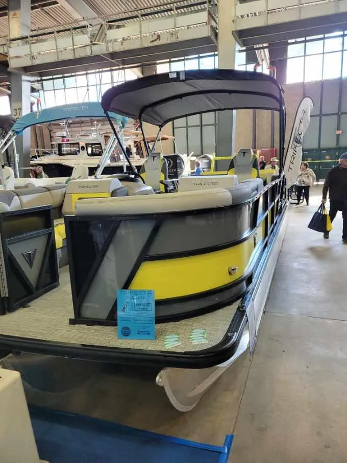Slide: The Image of 2023 Trifecta 23 UL SS pontoon boat with yellow accents displayed indoors. - 16