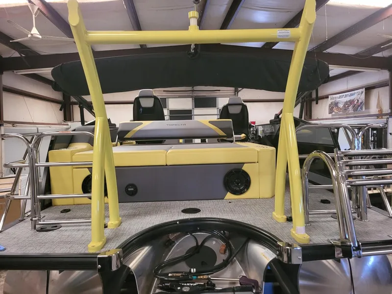 Slide: The Image of 2023 Trifecta 23 UL SS pontoon boat interior with yellow accents in a warehouse. - 6