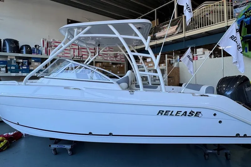 The Image of 2023 Release 230 DC boat in showroom, white exterior, flags, Yamaha engine visible. - 0