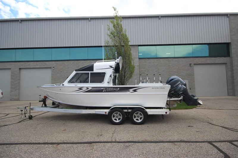 Slide: The Image of 2023 Weldcraft 210 Revolution F200XB Walleye Edition boat on trailer, parked outside a warehouse. - 0
