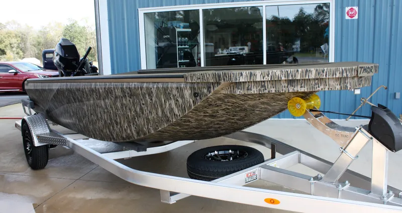 Slide: The Image of 2023 Thor Lake Hammer boat on trailer, camo design, parked outside blue building. - 6