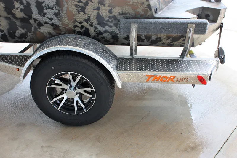 Slide: The Image of 2023 Thor Lake Hammer boat trailer with black alloy wheel and camouflage boat. - 12