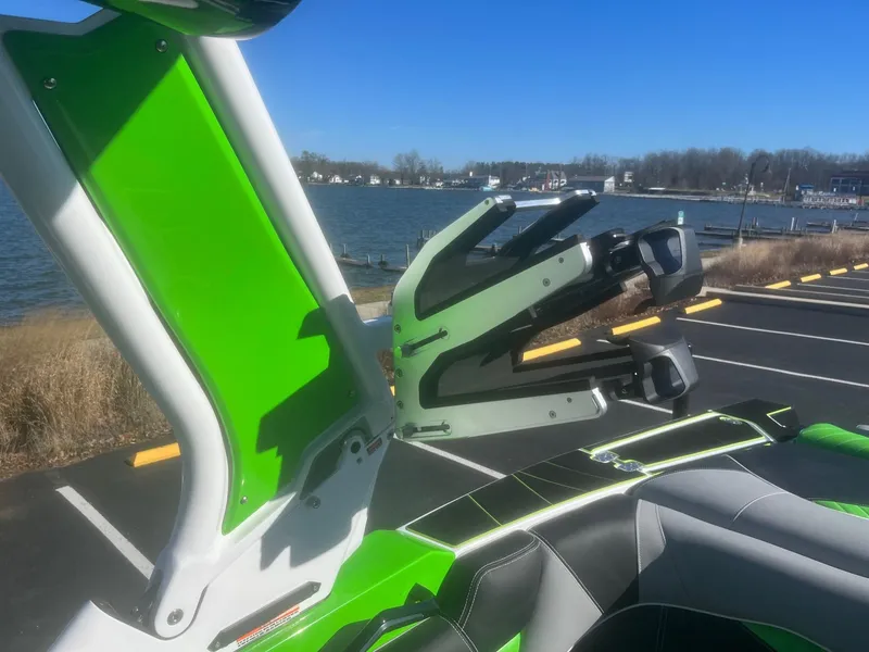 Slide: The Image of 2023 Centurion Fi23 boat with green accents, featuring a wakeboard rack by a lakeside. - 11