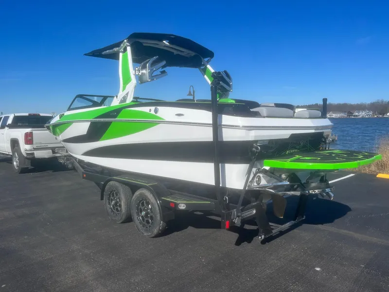 Slide: The Image of 2023 Centurion Fi23 boat with green accents on a trailer by a lake. - 3