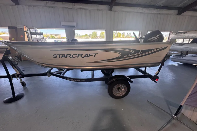 The Image of 2023 Starcraft Alaskan 12 boat on trailer in showroom, featuring Mercury engine. - 0